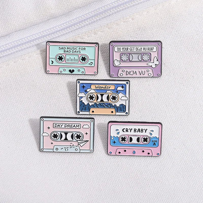 Five cassette tape-shaped pins with different designs and text on a white background