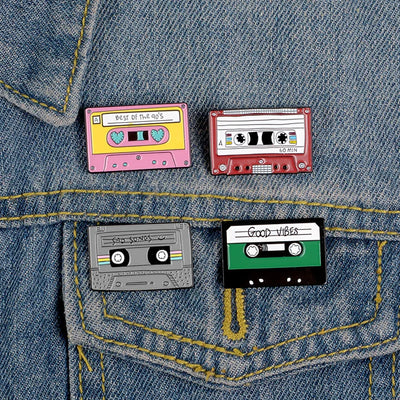 Four cassette tape-shaped pins on a denim background