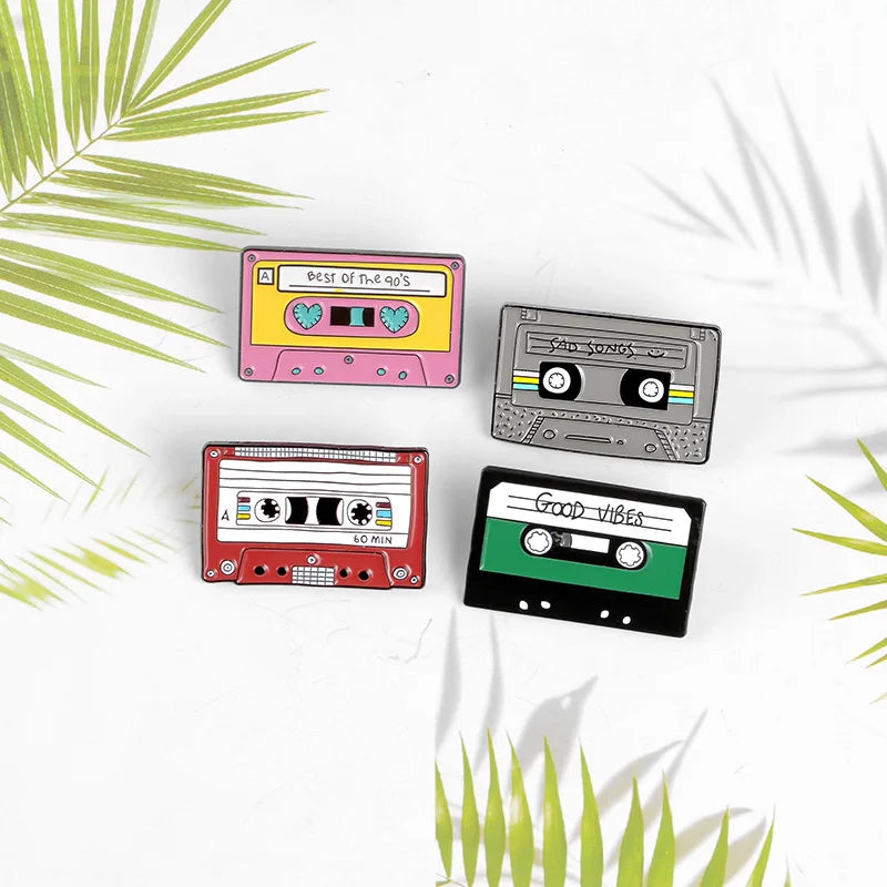 Four colorful cassette tape-shaped pins on a white background with green leaf patterns.
