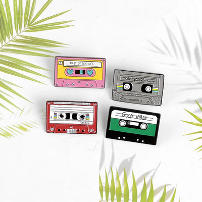 Four colorful cassette tape-shaped pins on a white background with green leaf patterns.