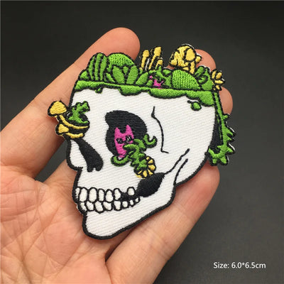 Skull patch with green leaves and pink flower held in a hand against a dark background
