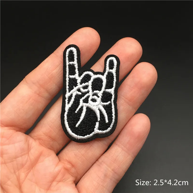 Hand holding a black and white embroidered patch of a hand making a rock sign against a dark background.