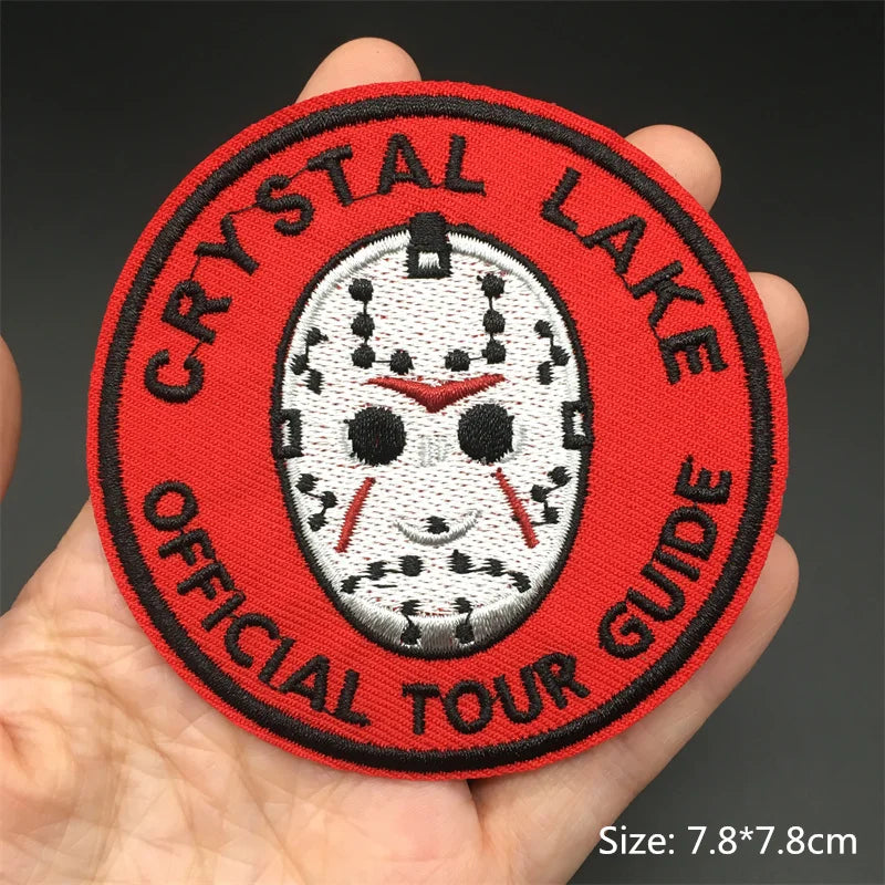 Round patch with 'Crystal Lake Official Tour Guide' text and a mask design held in a hand.