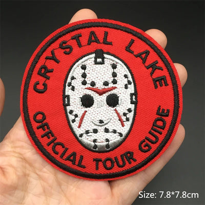 Round patch with 'Crystal Lake Official Tour Guide' text and a mask design held in a hand.