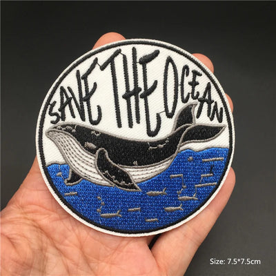 Patch with whale design and 'Save the Ocean' text held in a hand against a dark background
