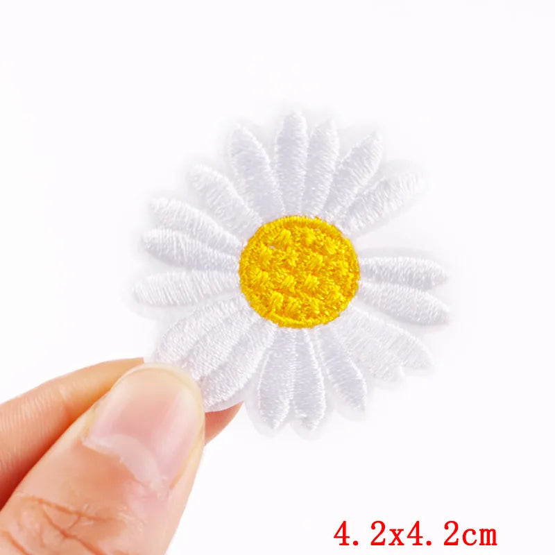 White embroidered flower patch held by a hand with a white background