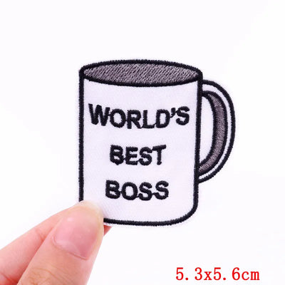 Embroidered patch of a mug with 'World's Best Boss' text held by a hand on a white background.