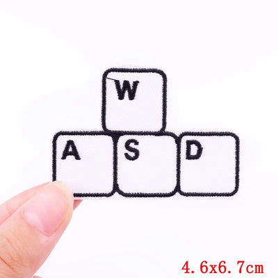 Keyboard key patch with 'WASD' letters held by a hand on a white background