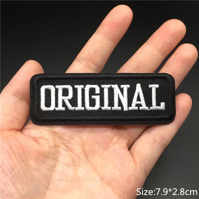 Black patch with 'ORIGINAL' text held in a hand against a dark background