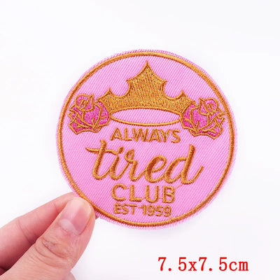 Pink patch with gold text and crown design held by a hand on a white background