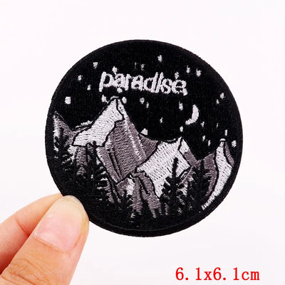 Round embroidered patch with a wolf howling at the moon and 'paradise' text, held by a hand.