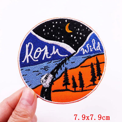 Embroidered patch with nature design and 'Roam Wild' text held by a hand.