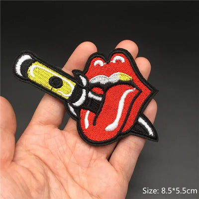 Embroidered patch of a tongue and knife design held in a hand with a dark background.