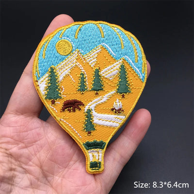 Embroidered patch of a mountain landscape held in a hand with a dark background