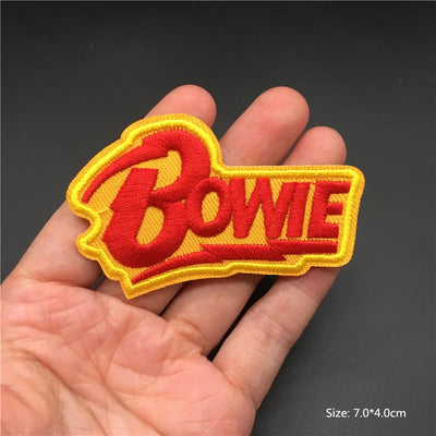 Red 'Bowie' patch with yellow border held in a hand against a dark background