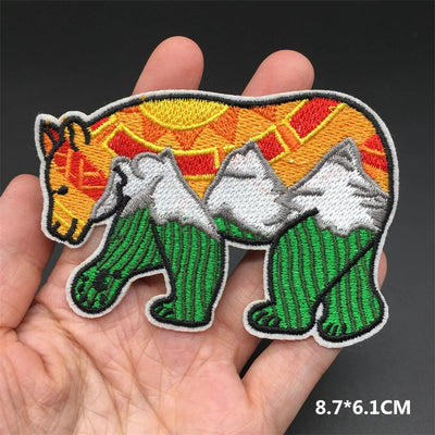 Embroidered patch of two bears with a colorful sun background held in a hand.