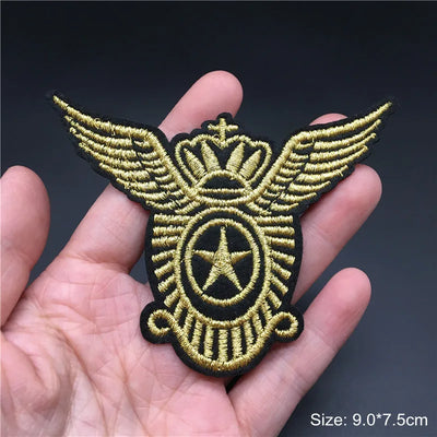 Gold and black embroidered patch with wings and star held in a hand against a dark background