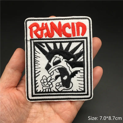 Patch with 'Rancid' logo held in a hand against a dark background