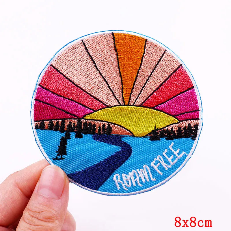 Circular patch with sunset design and 'Roam Free' text held by a hand on a white background
