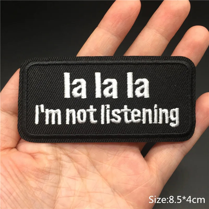 Black patch with 'la la la I'm not listening' text held in a hand against a dark background