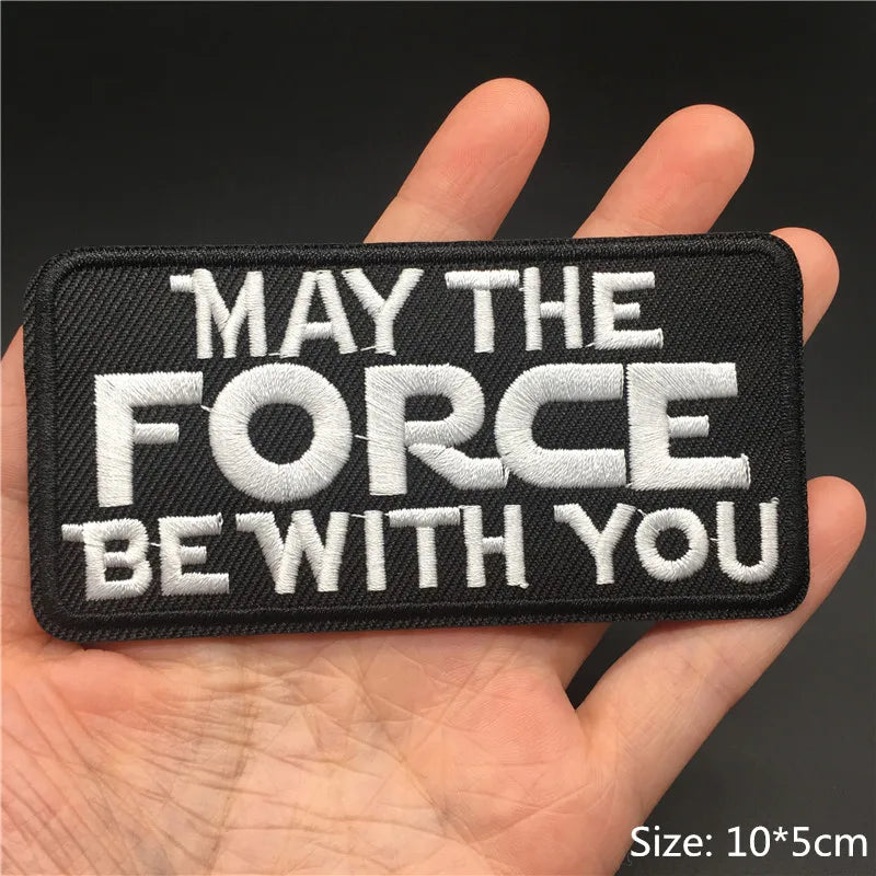 Embroidered patch with 'May the Force Be With You' text held in a hand against a dark background