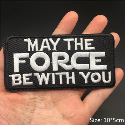 Embroidered patch with 'May the Force Be With You' text held in a hand against a dark background