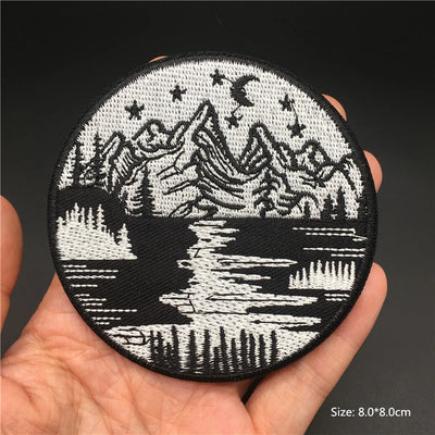 Embroidered patch with mountain and lake design held in a hand against a dark background