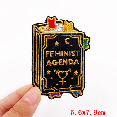 Patch with 'Feminist Agenda' text held by a hand on a white background
