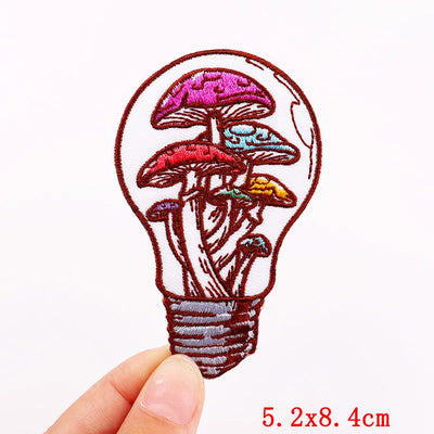 Embroidered patch of mushrooms inside a light bulb held by a hand on a white background.