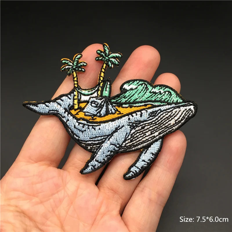 Embroidered patch of a whale with palm trees on a hand against a dark background
