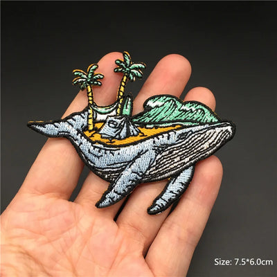 Embroidered patch of a whale with palm trees on a hand against a dark background