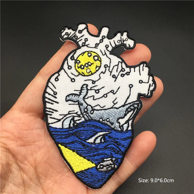 Embroidered patch of a wave with a moon and fish held in a hand against a dark background