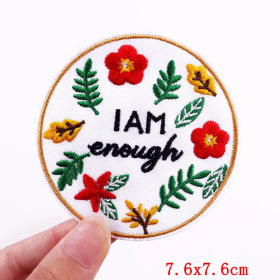 Circular patch with floral design and 'I AM enough' text held by a hand on a white background.