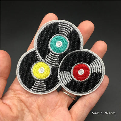 Three circular patches with colorful centers held in a hand against a dark background
