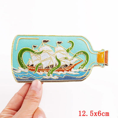 Embroidered patch of a ship in a bottle held by a hand on a white background