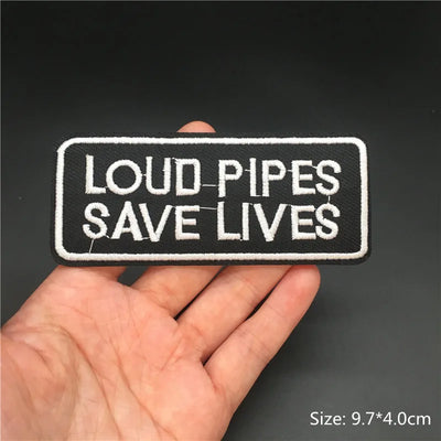 Patch with 'LOUD PIPES SAVE LIVES' text held in a hand against a dark background