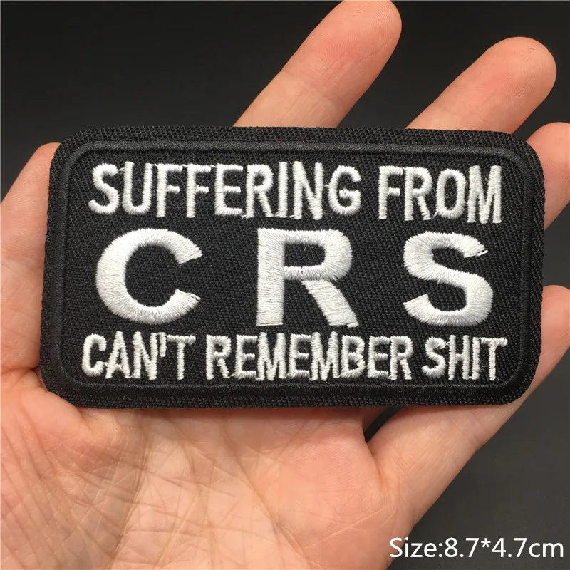 Patch with text 'SUFFERING FROM CRS CAN'T REMEMBER SHIT' held in a hand against a dark background