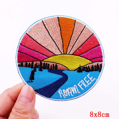 Circular patch with sunset design and 'Roam Free' text held by a hand on a white background