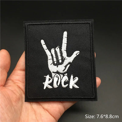 Black patch with white hand gesture and 'ROCK' text held in a hand against a dark background