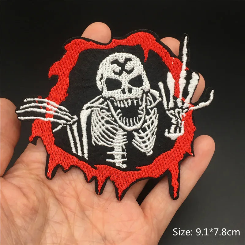 Embroidered skeleton patch with red border held in hand against a dark background