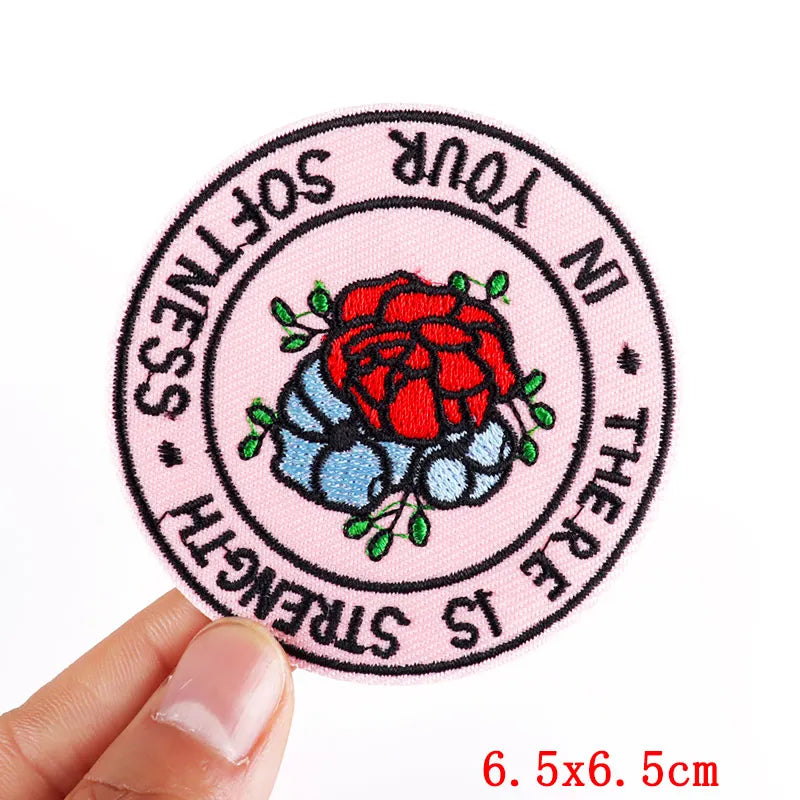Circular patch with a red rose and text held by a hand on a white background
