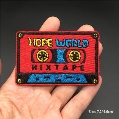Embroidered patch of a cassette tape with 'Hope World Hixtape' text held in a hand.