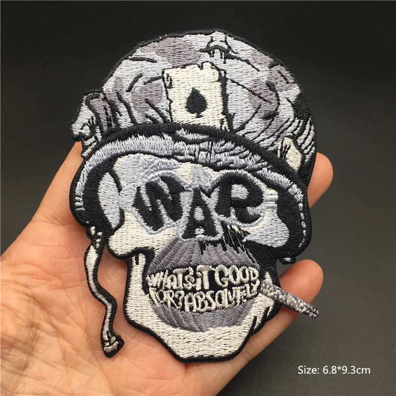 Embroidered patch with skull design and text held in a hand against a dark background