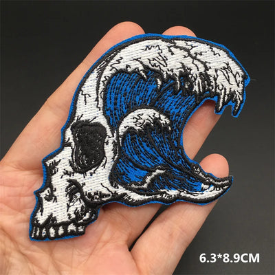 Embroidered patch of a skull with a wave design held in a hand, on a dark background.