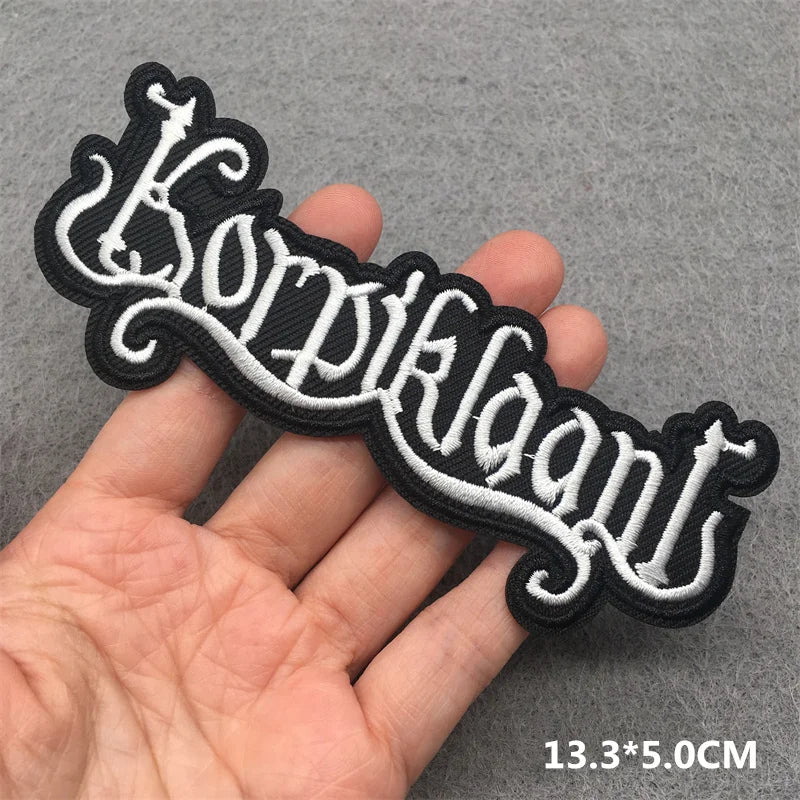 Black and white embroidered patch with decorative text held by a hand on a gray background