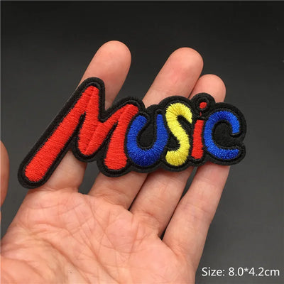Colorful 'Music' patch held between fingers against a dark background
