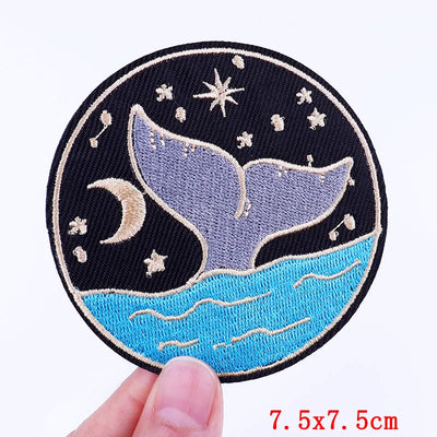 Embroidered patch with whale tail design held by a hand on a white background