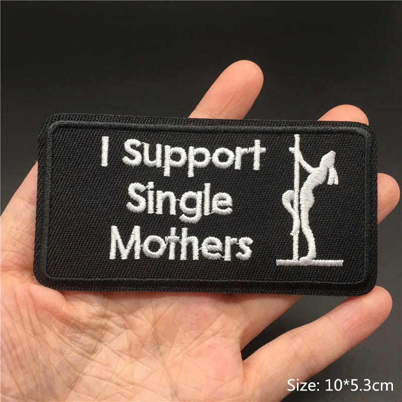 Patch with 'I Support Single Mothers' text and a pole dancer illustration held in a hand.