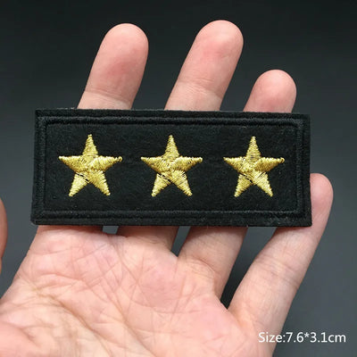 Black patch with three gold stars held in a hand against a dark background