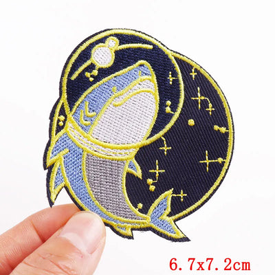 Embroidered patch of a shark with starry background held by a hand, size 6.7x7.2cm.